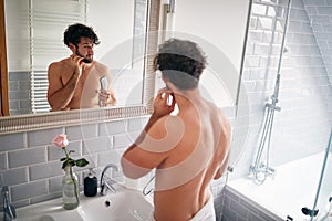 A young handsome guy cutting his beard in the bathroom. Hygiene, bathroom, morning