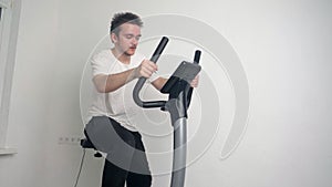 Young handsome guy doing sports at home, he is sitting on a stationary bike