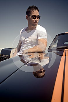 Young handsome guy leaning on muscle car with stripes