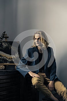 Young handsome guy with long blonde hair in a blue jacket poses
