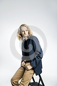Young handsome guy with long blonde hair in a blue jacket poses, isolated