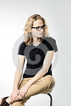 A young handsome guy with long blonde hair and glasses looks away