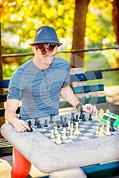 A young handsome guy is playing chess outside in golden autumn afternoon