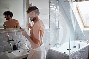 A young handsome guy posing for a photo while cutting his beard and in the bathroom. Hygiene, bathroom, morning