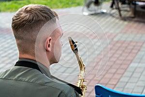 A young handsome guy with a saxophone in his hands. A military band, a musician in a military uniform holding an instrument. Wind