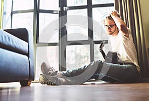 Young handsome guy sits on floor iat home and plays on guitar