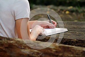 Young handsome guy sitting at wooden table, writing a book, doing homework, taking notes, learning, contemplating and writing.