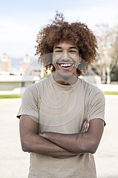 Young handsome guy smiling relaxed and looking at camera in the street with arms crossed. Confident happy man laughing