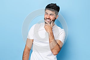 Young handsome guy wearing a white t-shirt, holds his hand at his chin