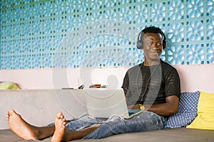 Young handsome and happy hipster black African American business man working with laptop computer and headphones smiling satisfied