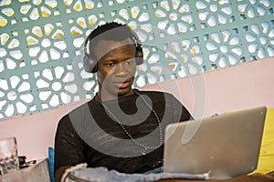 Young handsome and happy hipster black African American business man working with laptop computer and headphones smiling satisfied