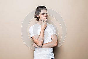 Young handsome happy man standing hand on chin looking up thinking on an beige background