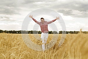 Young handsome happy man standing in wheat field spreading his arms up