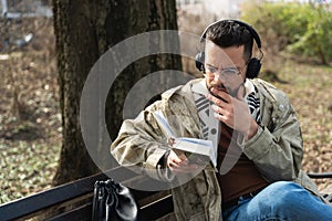 Young handsome hipster freelance business man wearing jacket reading a book while sitting outdoors. Businessperson on lunch break