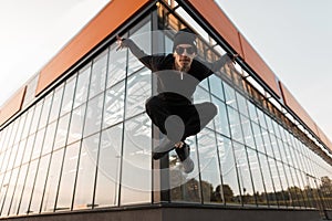 Young handsome hipster man in black fashionable clothes in a stylish hat in fashionable sneakers in sunglasses is jumping