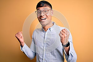 Young handsome hispanic business man wearing nerd glasses over yellow background celebrating surprised and amazed for success with