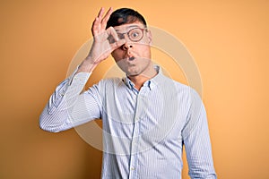 Young handsome hispanic business man wearing nerd glasses over yellow background doing ok gesture shocked with surprised face, eye