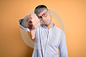 Young handsome hispanic business man wearing nerd glasses over yellow background looking unhappy and angry showing rejection and