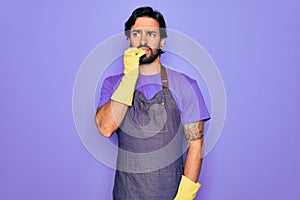 Young handsome hispanic clenaer man wearing housework apron and washing gloves looking stressed and nervous with hands on mouth