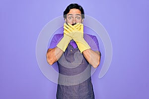 Young handsome hispanic clenaer man wearing housework apron and washing gloves shocked covering mouth with hands for mistake