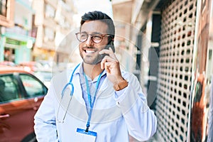 Young handsome hispanic doctor wearing stethoscope smiling happy Standing with smile on face talking on the smartphone at town
