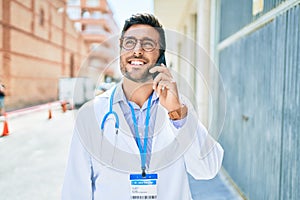 Young handsome hispanic doctor wearing stethoscope smiling happy Standing with smile on face talking on the smartphone at town