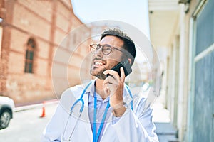 Young handsome hispanic doctor wearing stethoscope smiling happy Standing with smile on face talking on the smartphone at town