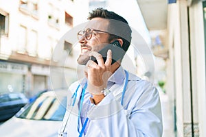 Young handsome hispanic doctor wearing stethoscope smiling happy Standing with smile on face talking on the smartphone at town