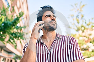 Young handsome hispanic man with beard smiling happy outdoors speaking on the phone