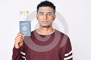 Young handsome hispanic man holding boarding pass and passport thinking attitude and sober expression looking self confident