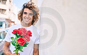 Young handsome hispanic man holding bouquet of roses leaning on the wall at street of city