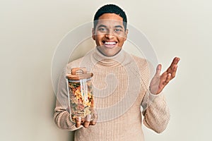 Young handsome hispanic man holding jar with farfalle pasta celebrating achievement with happy smile and winner expression with