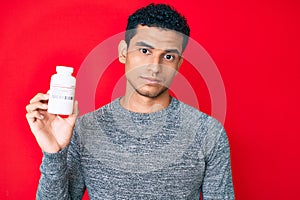 Young handsome hispanic man holding pills thinking attitude and sober expression looking self confident