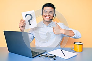 Young handsome hispanic man holding question mark as customer support smiling happy and positive, thumb up doing excellent and