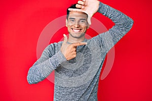 Young handsome hispanic man over red background smiling making frame with hands and fingers with happy face