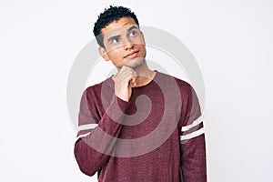 Young handsome hispanic man over white background thinking concentrated about doubt with finger on chin and looking up wondering