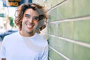 Young handsome hispanic man smiling happy leaning on the wall at street of city