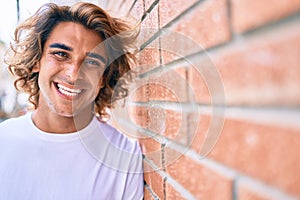 Young handsome hispanic man smiling happy leaning on the wall at street of city