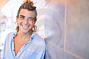 Young handsome hispanic man smiling happy leaning on the wall at street of city