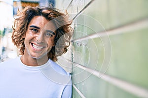 Young handsome hispanic man smiling happy leaning on the wall at street of city