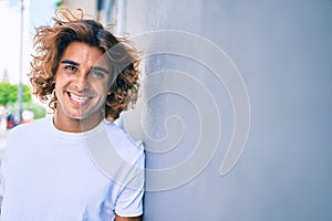 Young handsome hispanic man smiling happy leaning on the wall at street of city