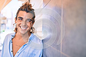 Young handsome hispanic man smiling happy leaning on the wall at street of city