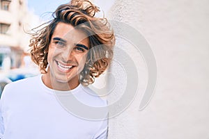 Young handsome hispanic man smiling happy leaning on the wall at street of city