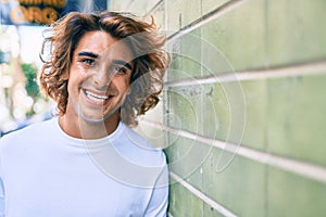 Young handsome hispanic man smiling happy leaning on the wall at street of city