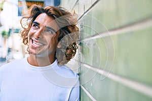 Young handsome hispanic man smiling happy leaning on the wall at street of city