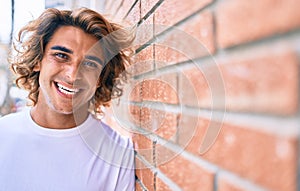 Young handsome hispanic man smiling happy leaning on the wall at street of city