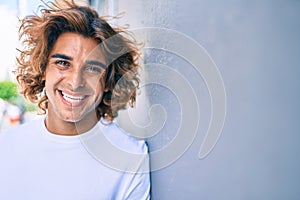 Young handsome hispanic man smiling happy leaning on the wall at street of city