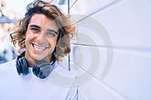 Young handsome hispanic man using headphones leaning on the wall at street of city