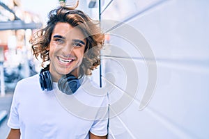 Young handsome hispanic man using headphones leaning on the wall at street of city