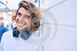 Young handsome hispanic man using headphones leaning on the wall at street of city